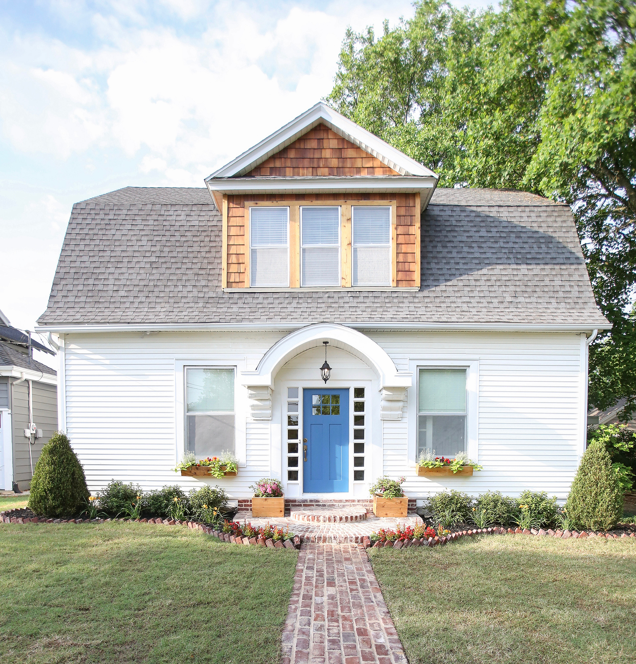 Reclaimed brick walkway lead to a home exterior with cedar shingle dormer on HGTV Fixer to Fabulous.