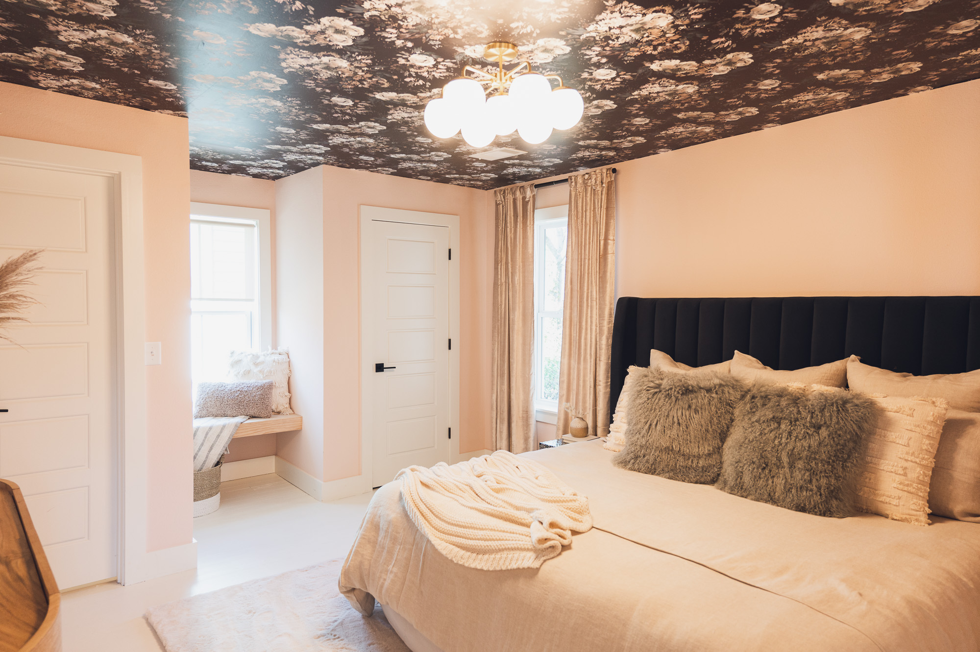 Light pink bedroom with window seat and dark, floral wallpaper on ceiling