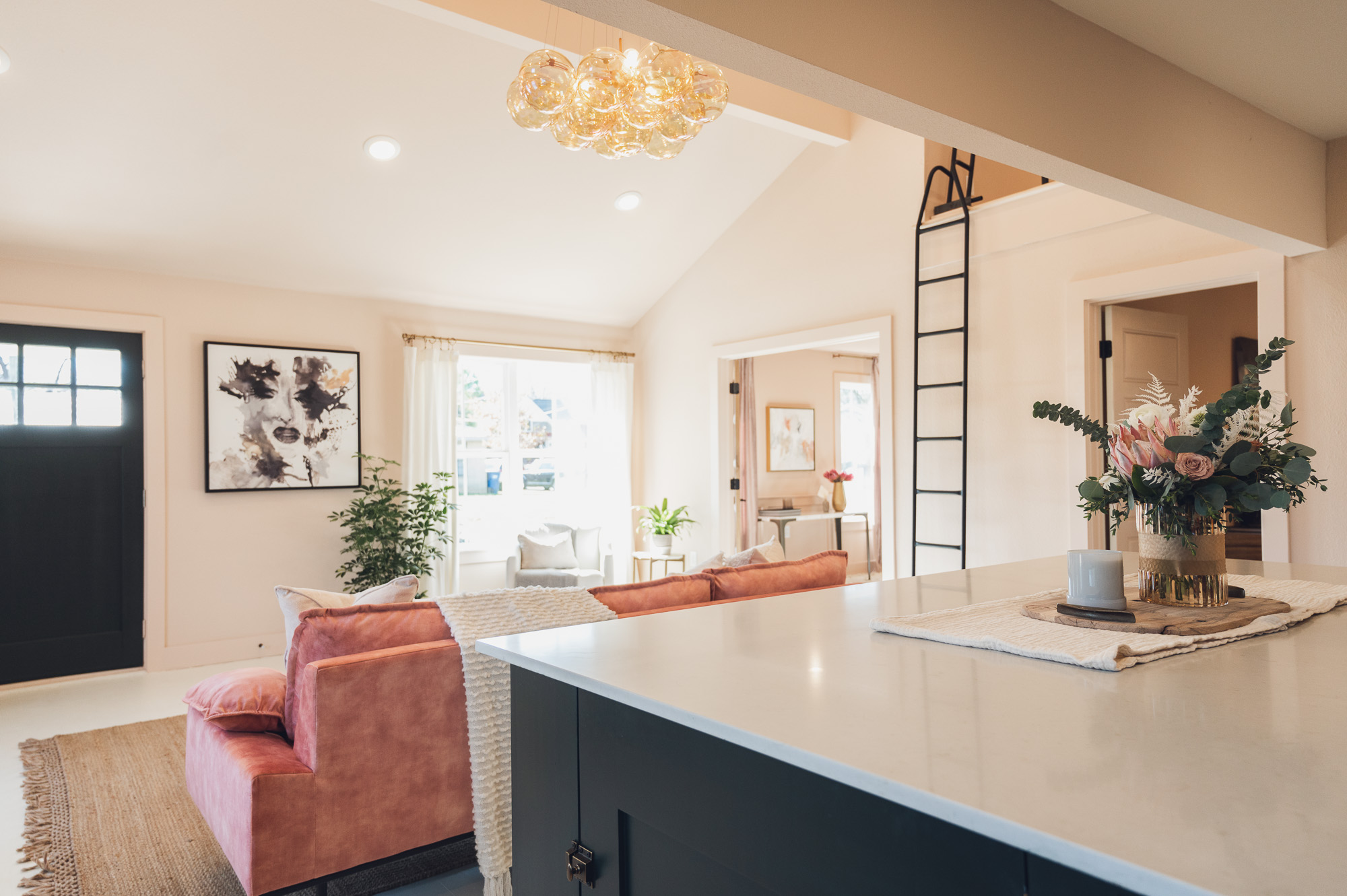 View from dark green kitchen island of remodeled living area with pink furniture